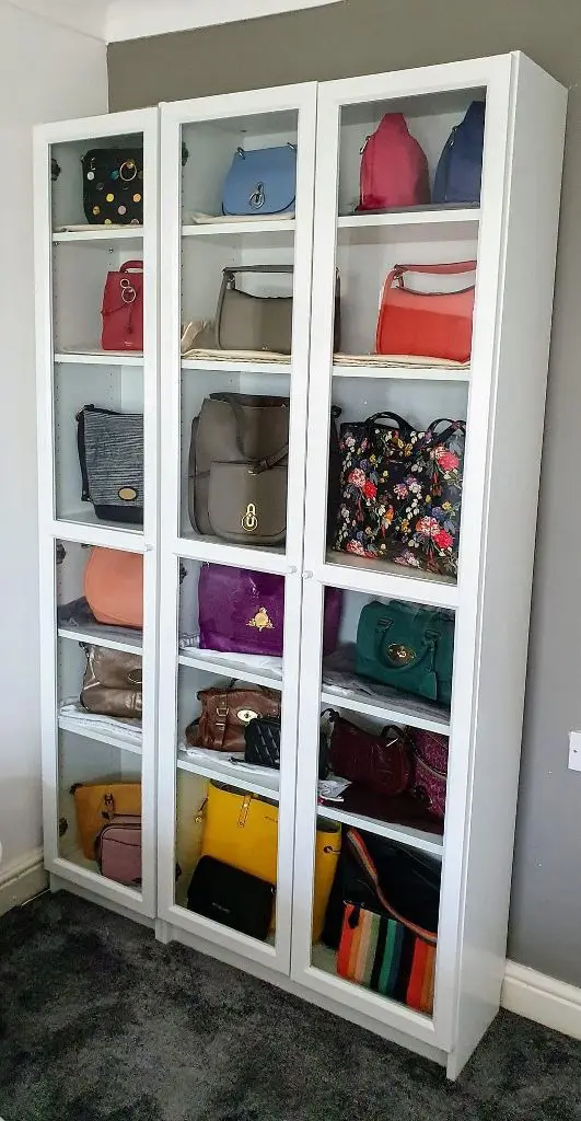 Three tall white glass front cabinets displaying a colorful collection of handbags on shelves.