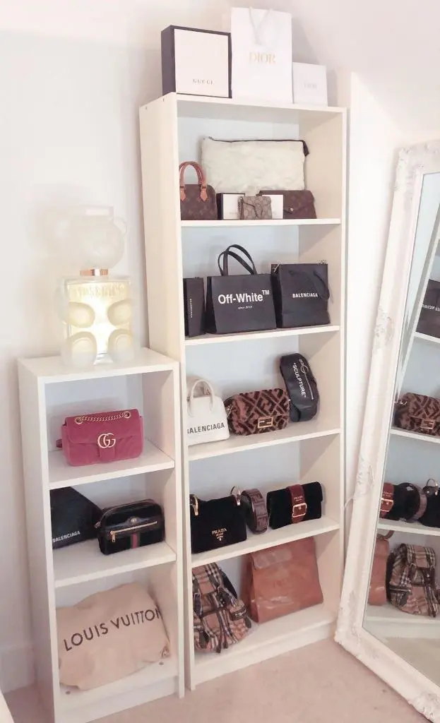Two white open shelving units filled with handbags, shopping bags, decor, and a large mirror.
