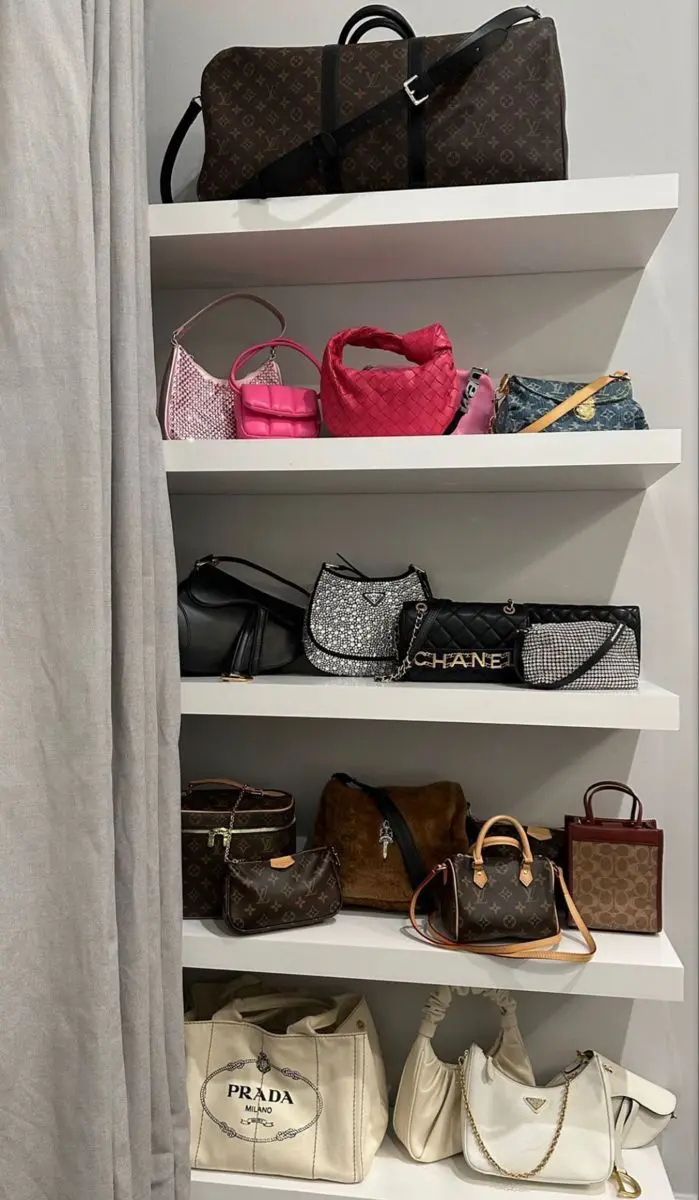 Multi tier white shelving unit filled with handbags of various colors, materials, and sizes.