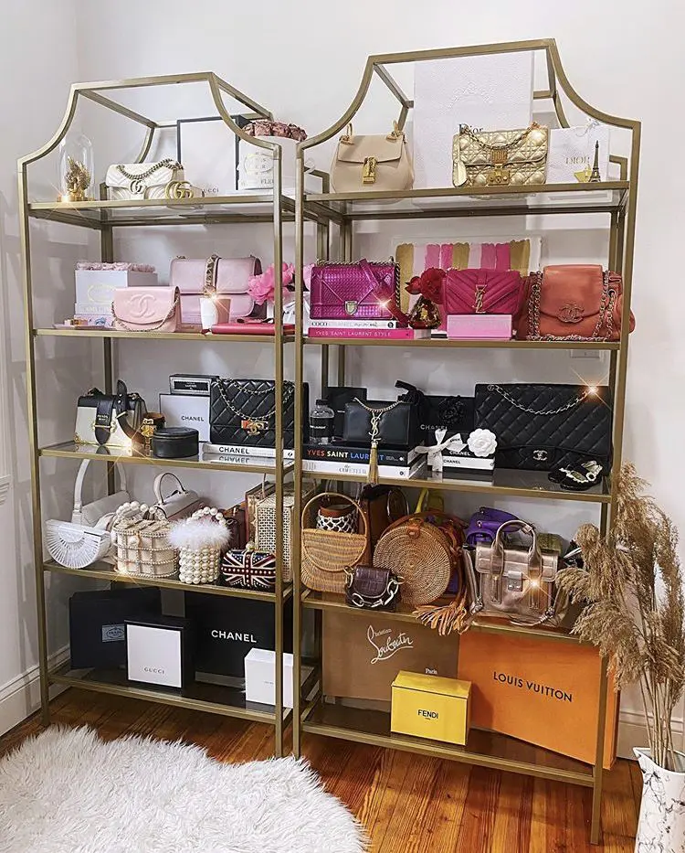 Gold metal shelving units with glass shelves displaying luxury handbags and decor items.