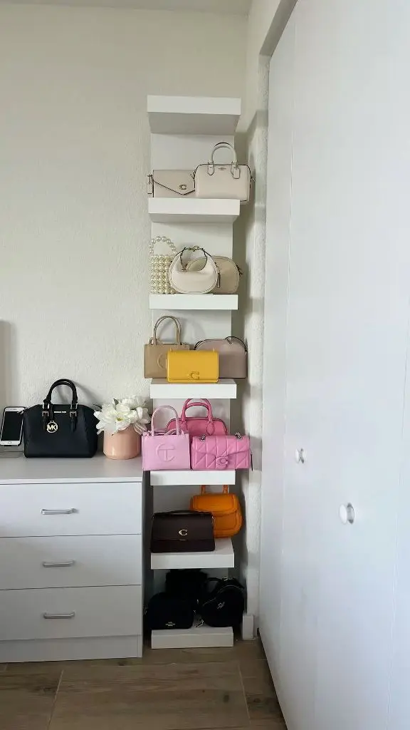 Vertical stack of white floating shelves displaying handbags above a white dresser.