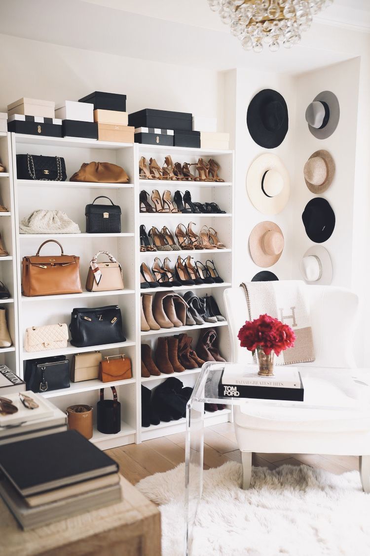 Bright boutique style wardrobe with white shelves, shoes, hats, handbags, armchair, and chandelier.