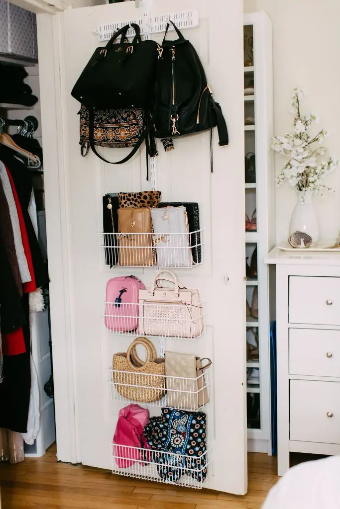 Over the door organizer with wire baskets and hooks holding handbags and accessories.