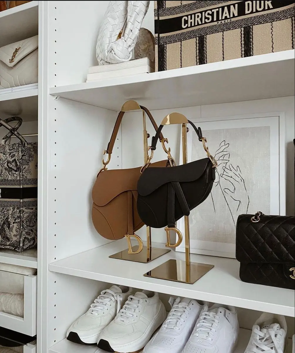 Two gold purse stands displaying luxury handbags on a white shelf with decor.