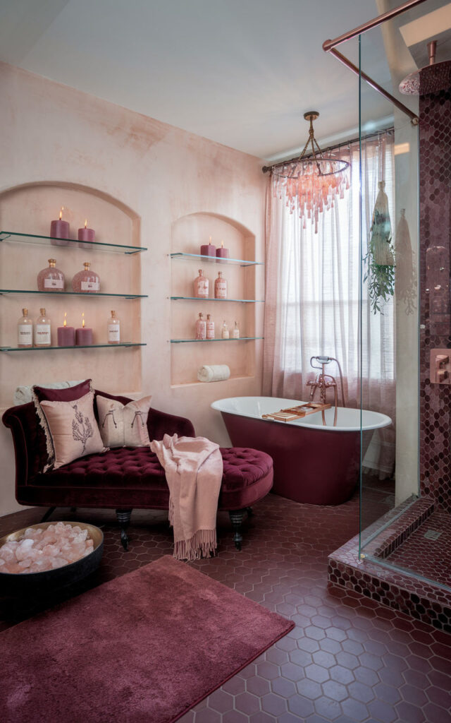 Mauve bathroom with a bathtub, candlelight, fluffy towels, a blanket draped over the tub edge, and fresh flowers.