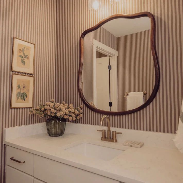 Soft pink and white striped wallpaper in a small bathroom with a round mirror and clean white fixtures.