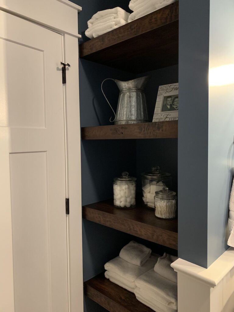 Bathroom with open wood shelving styled with brown decor and plants