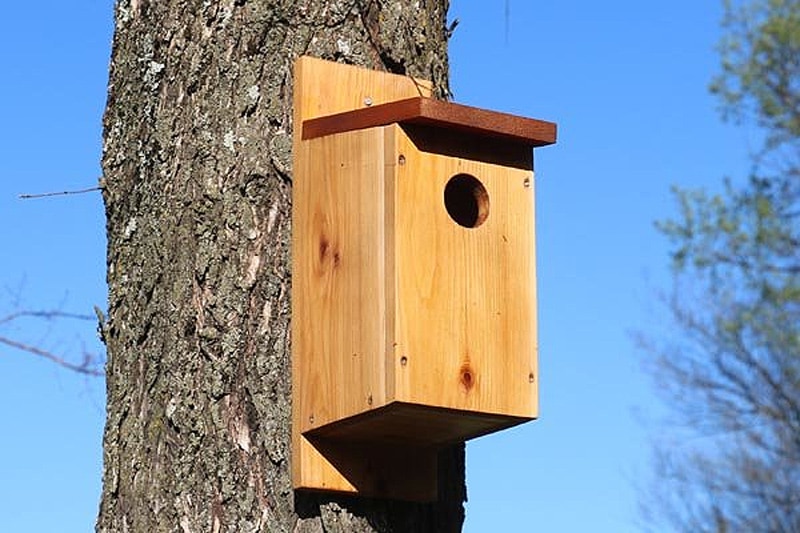 Birdhouse covered in wine corks forming a mosaic texture with a dark wood roof.