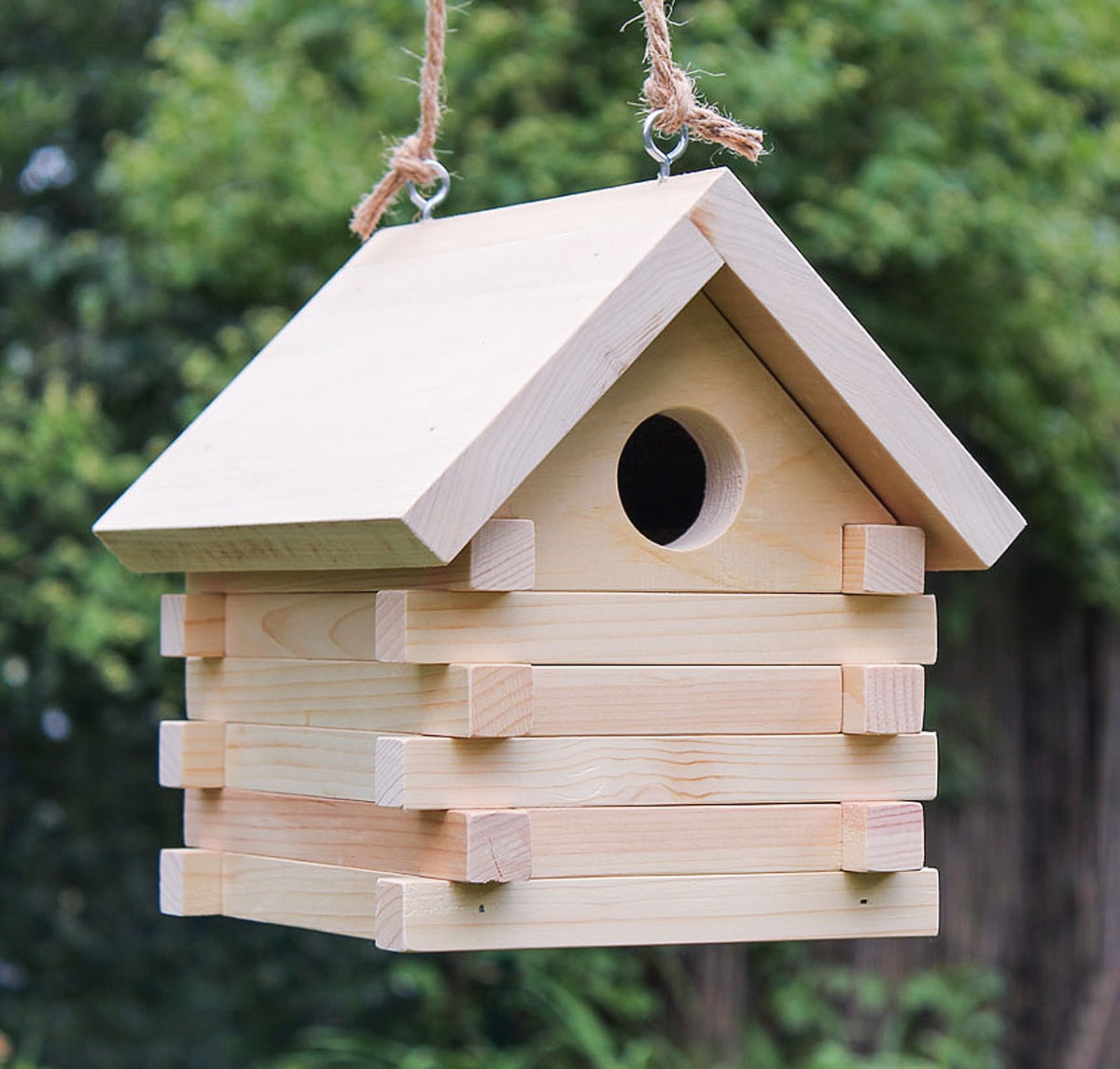 Teal painted birdhouse with natural wood perch mounted on a fence.