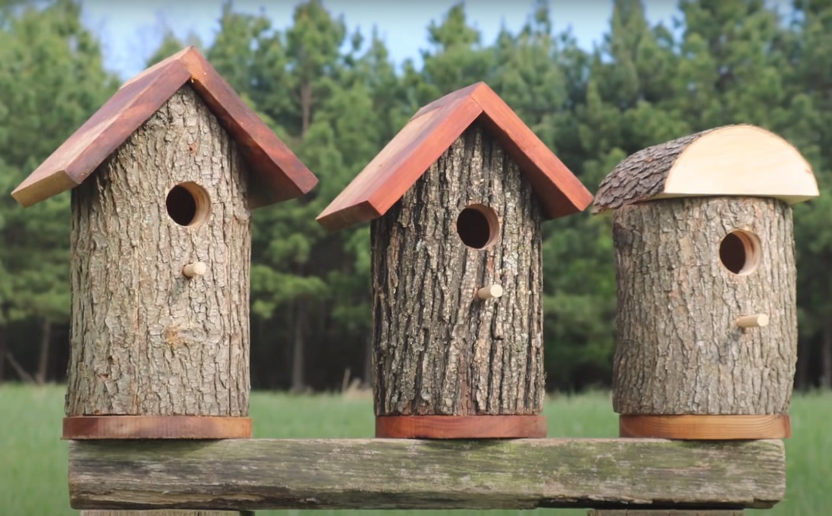 European style birdhouse covered in smooth river stones with a dark shingled roof.