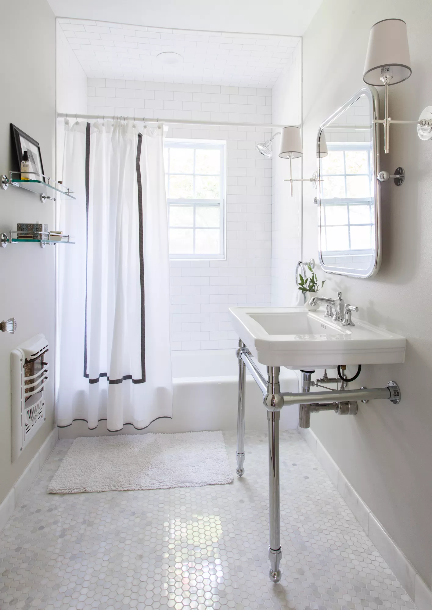 White subway tile shower with a chrome console sink, bright window light, hexagon floor tiles, and a white shower curtain with black trim.