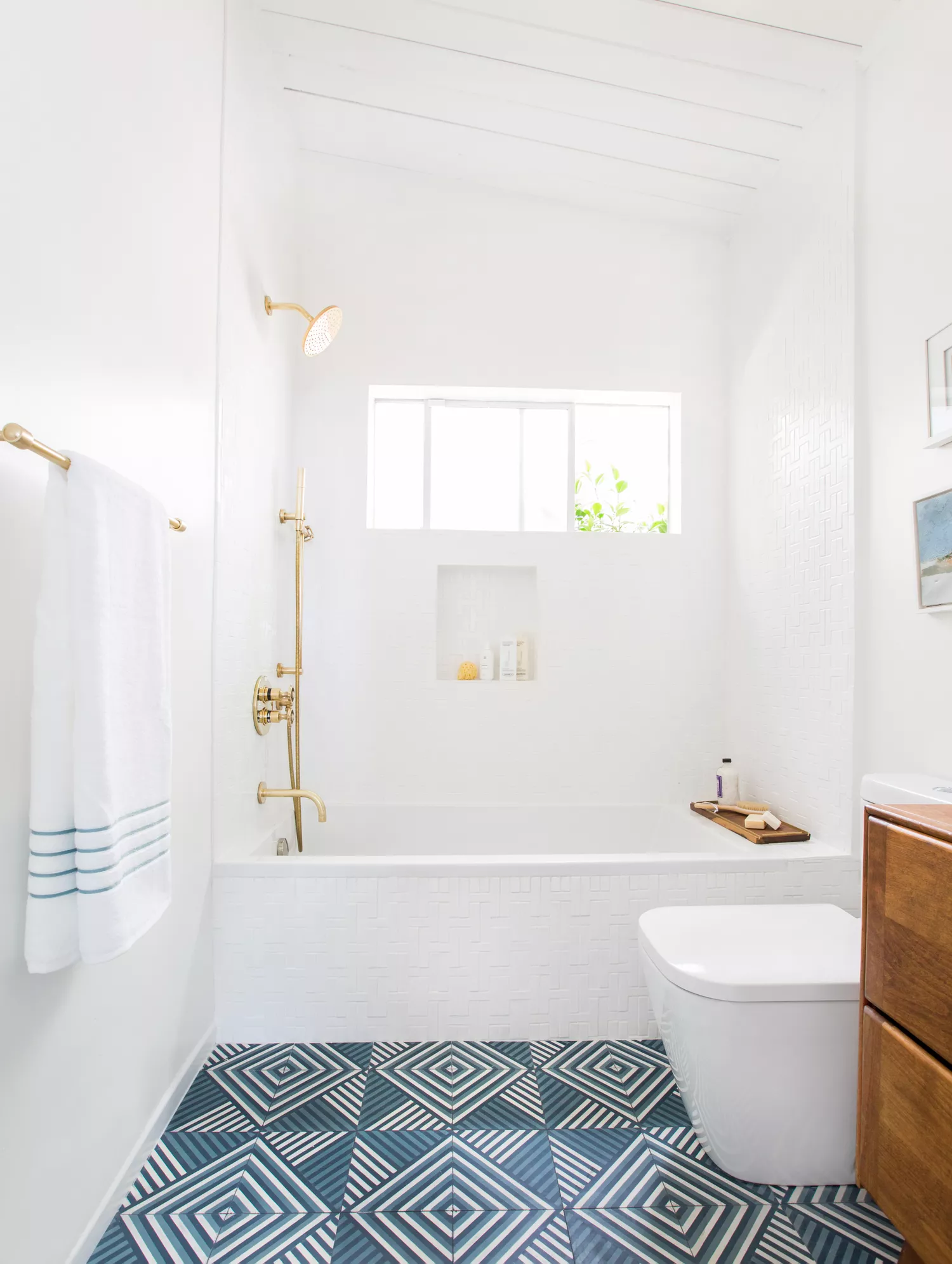 Modern bathroom with a built-in tub, brushed gold hardware, white walls, floating toilet, and bold blue geometric floor tile.