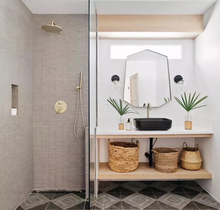 Bathroom with a walk-in shower of vertical gray tiles, a floating wood vanity shelf, woven baskets underneath, and a black vessel sink.