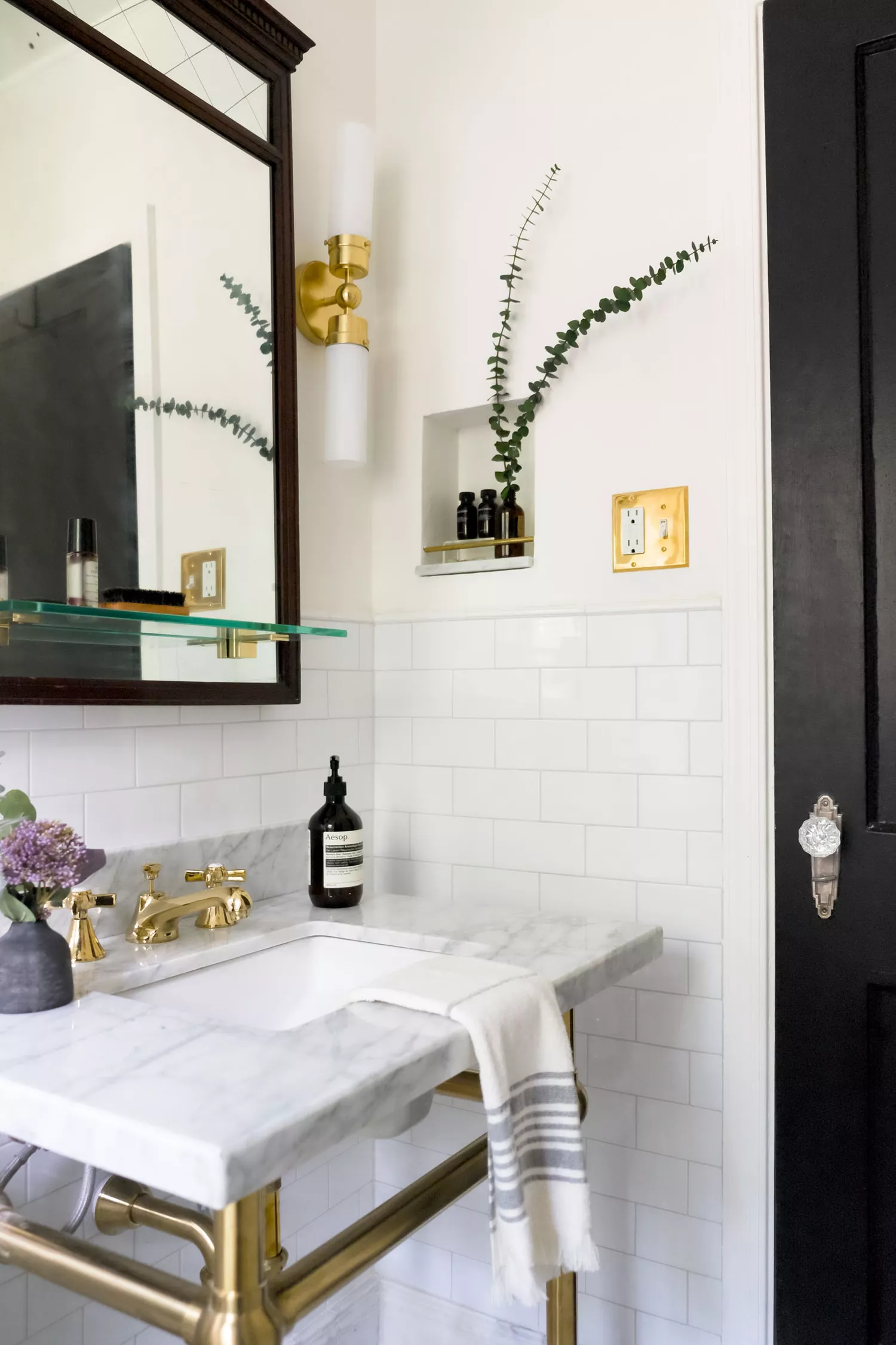 Moody powder room with dark floral wallpaper, brass mirror, and ornate brass sconces.