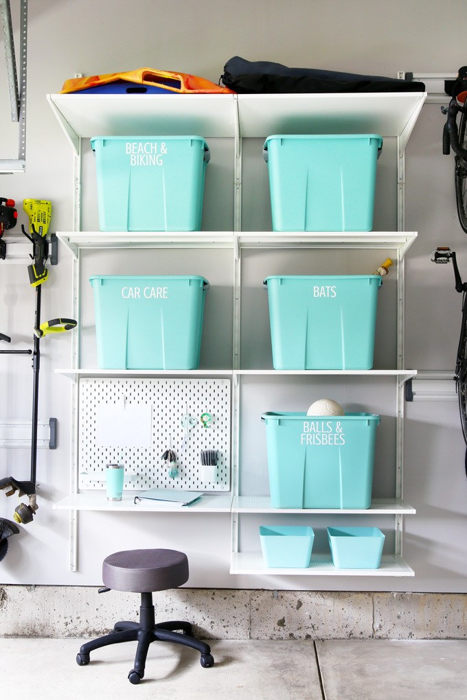 Teal storage bins on white garage shelving organized by category
