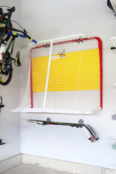 Hockey net and sticks mounted vertically on garage wall hooks