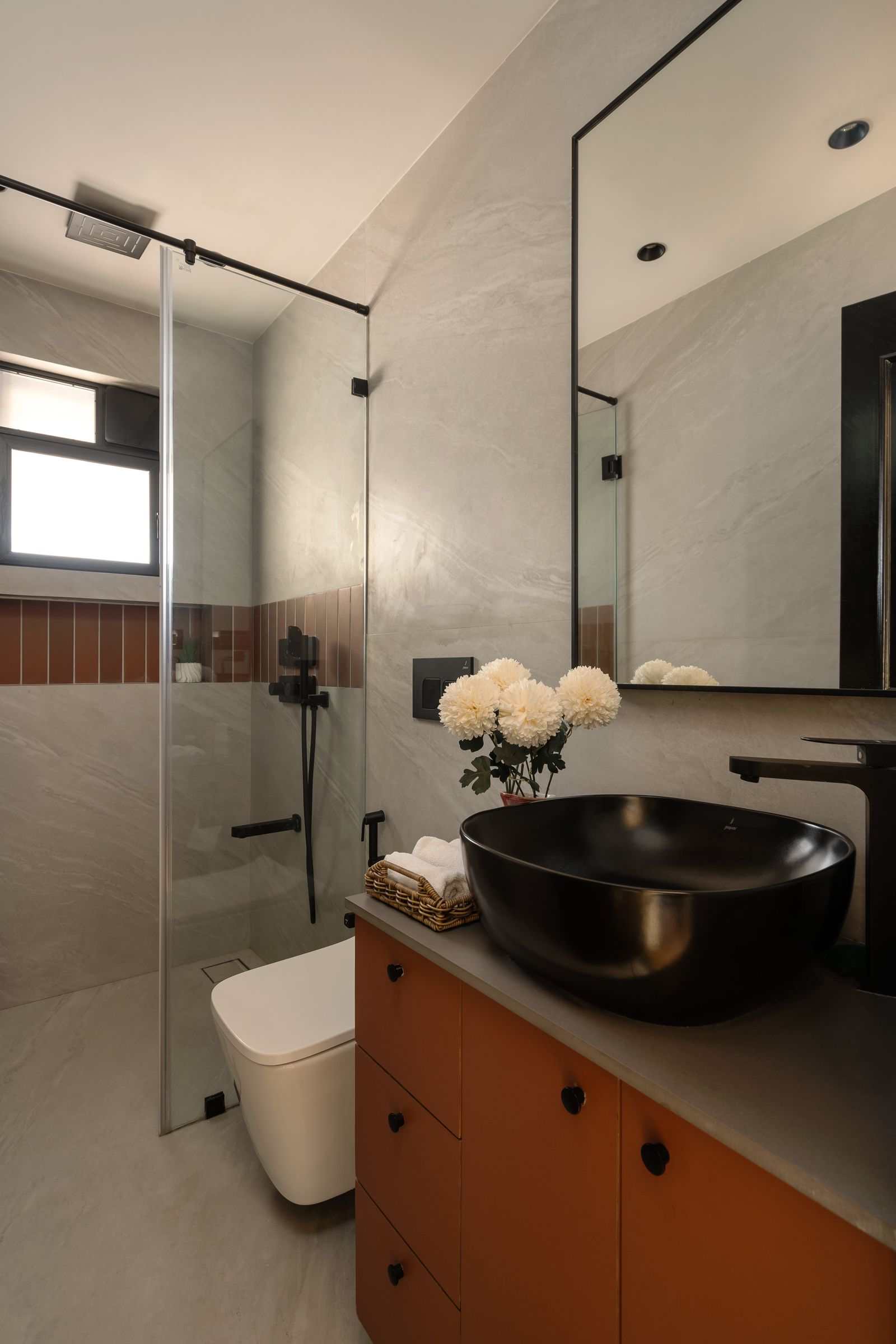 Small wet room bathroom with gray stone tiles on walls and floor, terracotta vanity, matte black vessel sink, black fixtures, and a frameless glass shower partition.