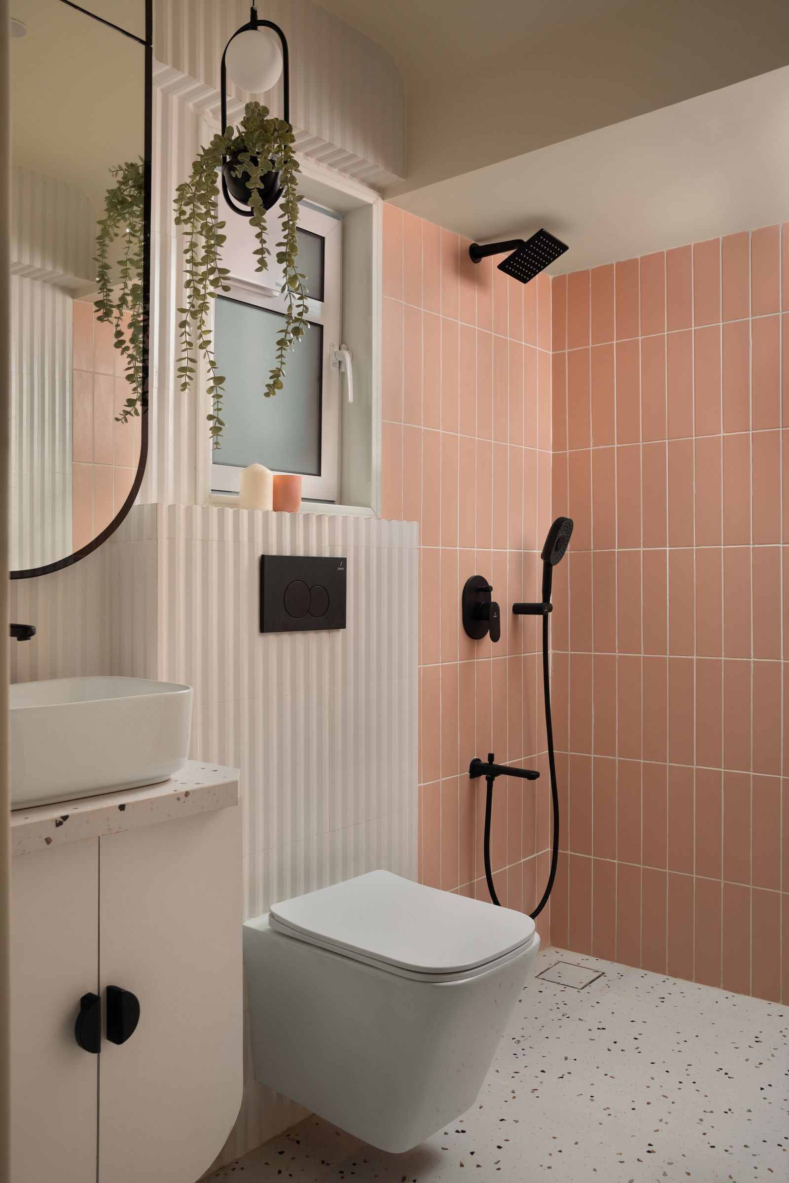 Small bathroom with vertical peach subway tiles in the shower, terrazzo flooring, wall-hung toilet with fluted panel concealment, and matte black fixtures.