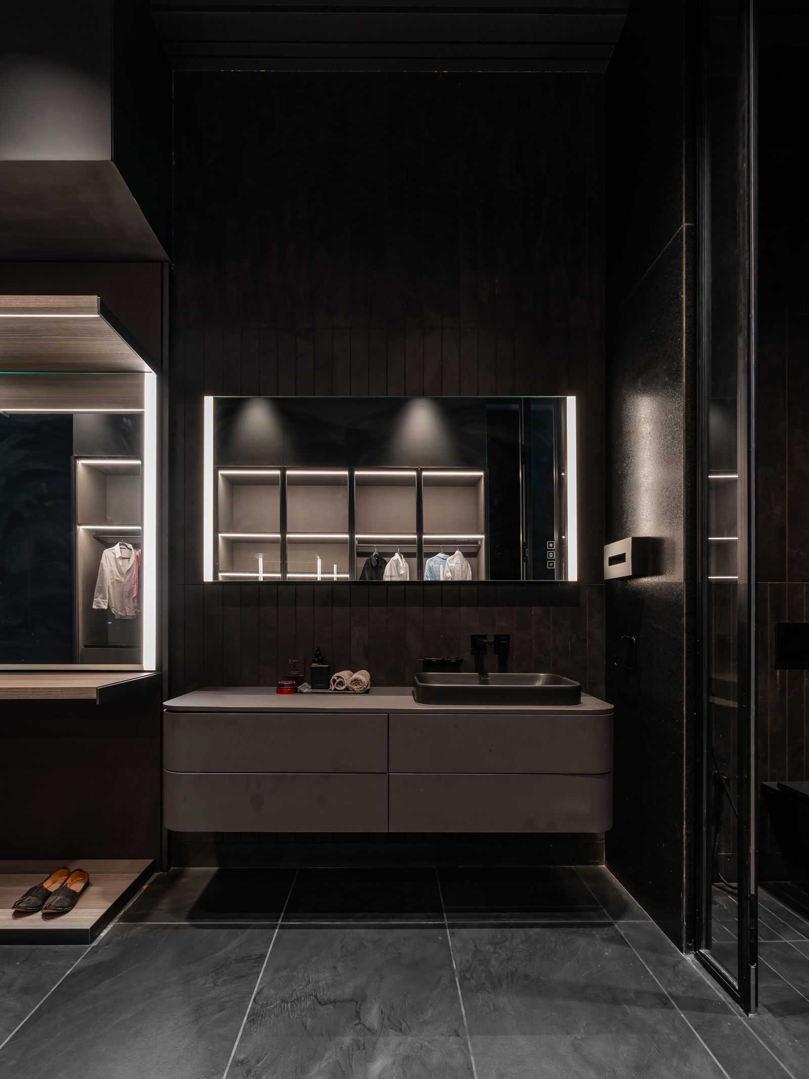 Small bathroom with a wide floating taupe vanity, dark vertical wall paneling, oversized backlit mirror, and integrated lighting for a soft glow.