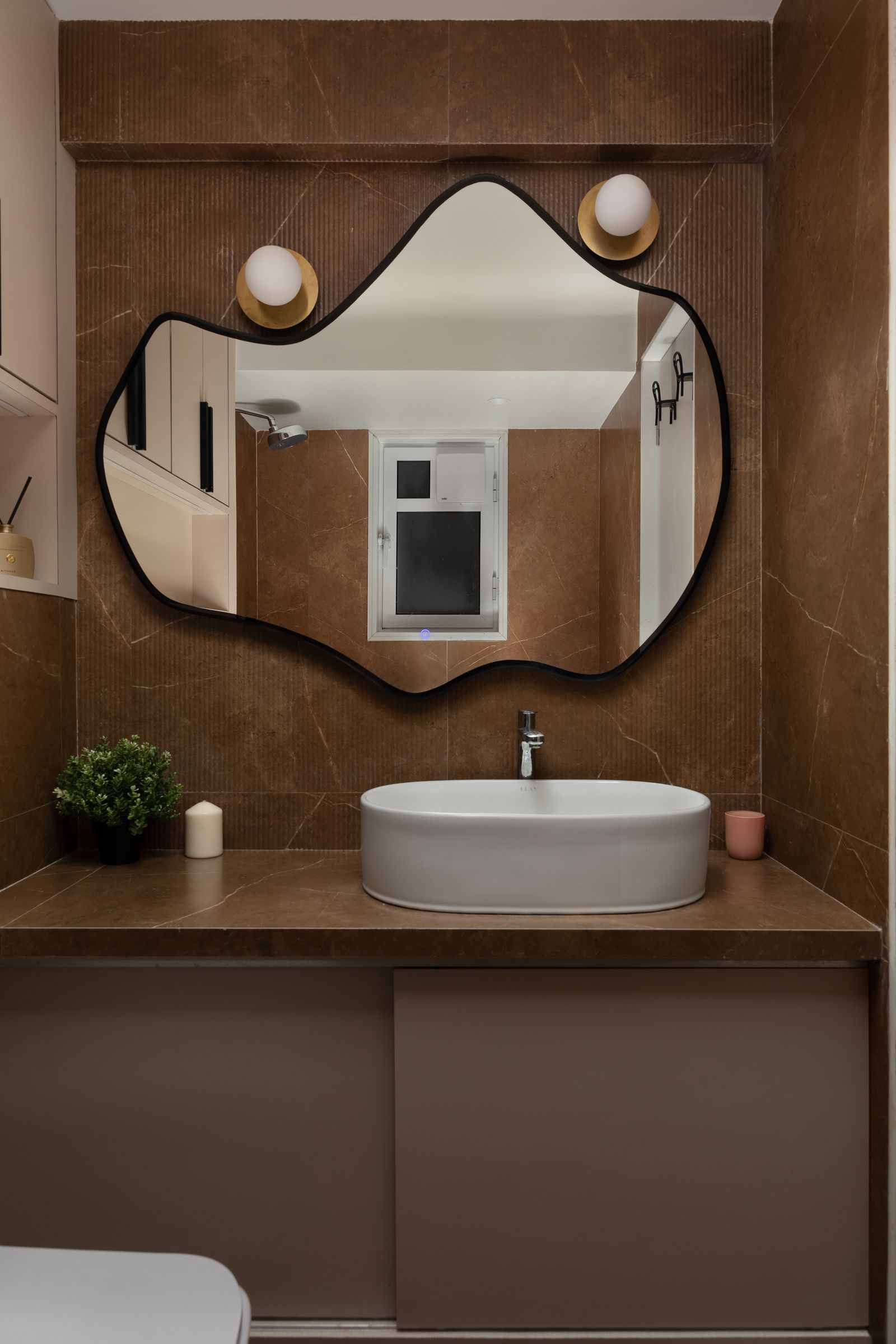 Small bathroom with arched shower entrance in terracotta tile, pale plaster walls, minimalist wood vanity with stone top, and warm lighting with organic accessories.