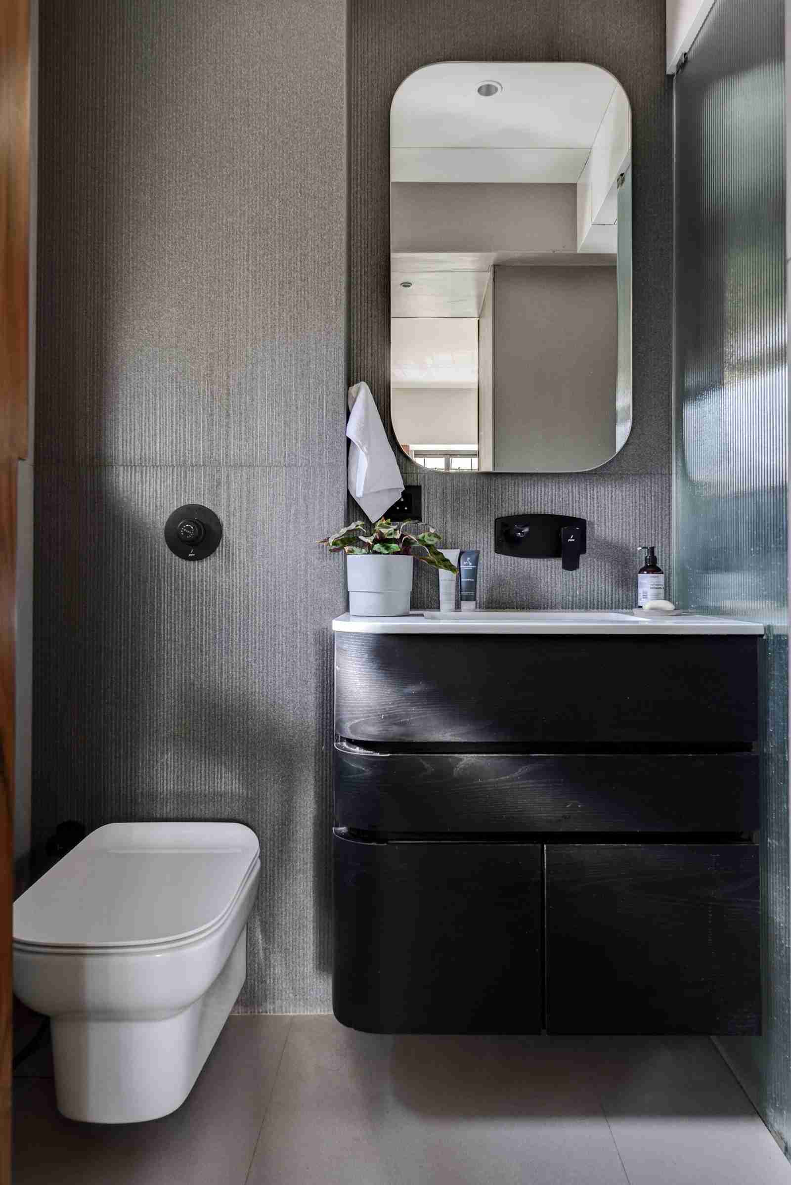 Small bathroom with reclaimed-style wood vanity, sandy textured stone tiles on walls, tall mirror framed with vertical wood planks, and black faucet.