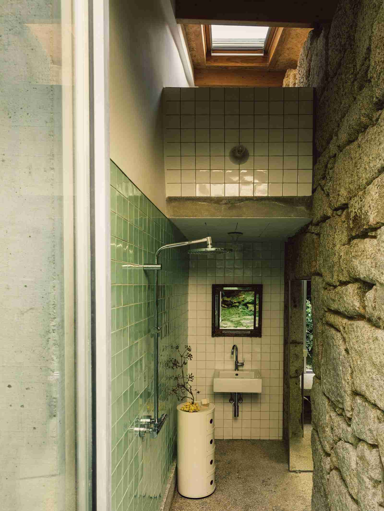 Minimalist wet room with concrete-look tiles on walls and floor, wall-mounted shower head, built-in bench, and a high narrow window bringing in soft light.