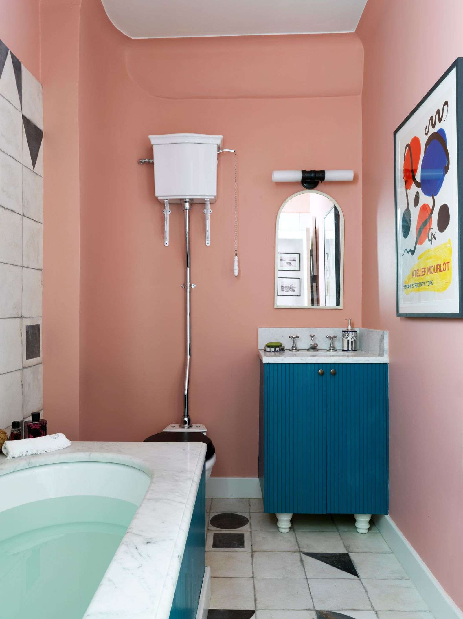 Small bathroom with teal vanity, gold hardware, white vertical wall tiles, round mirror, and globe sconces with mid-century style.
