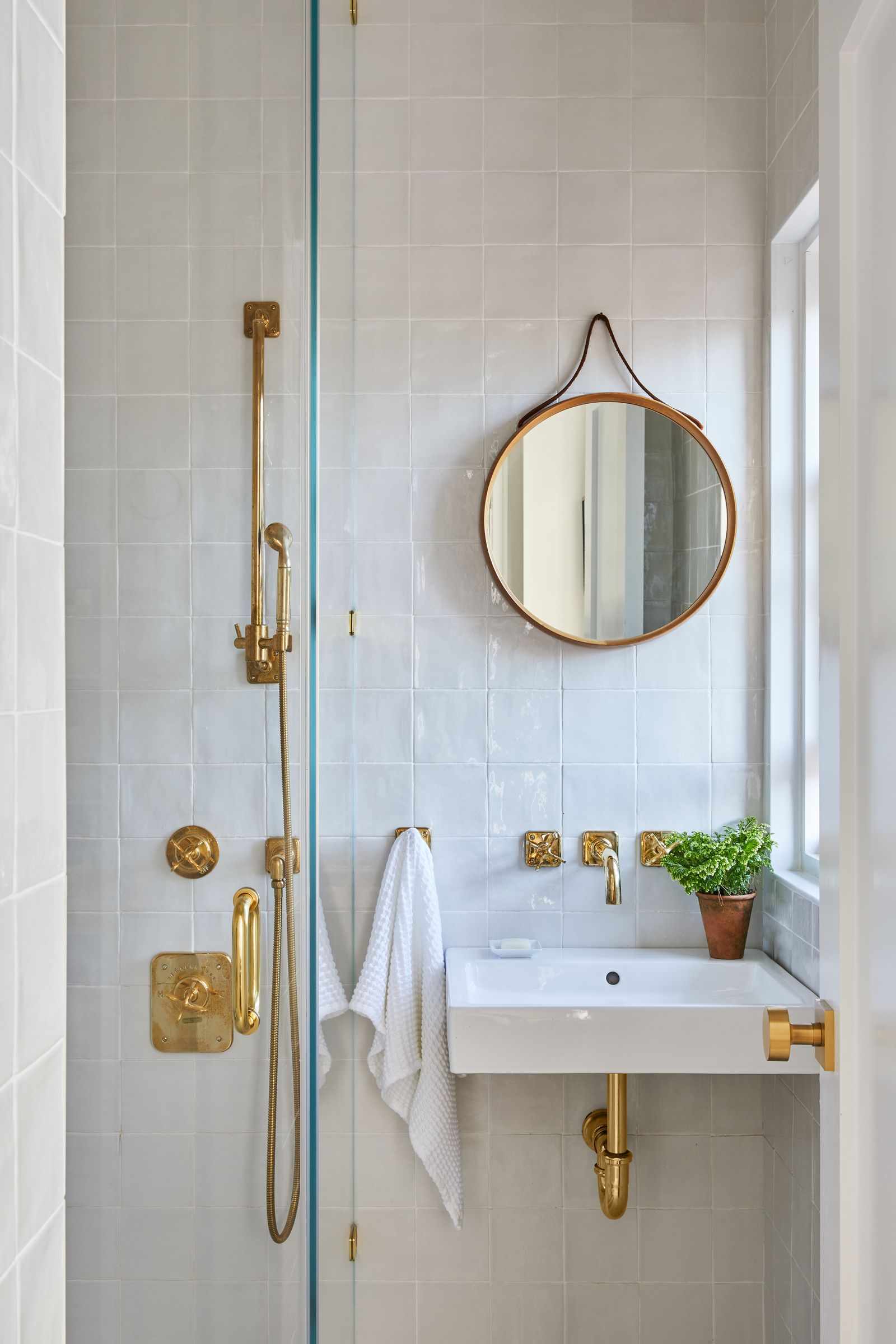 Small bathroom with black-framed glass shower partition, light gray stone tiles, floating wood shelf vanity, white vessel sink, and wall-mounted faucet.