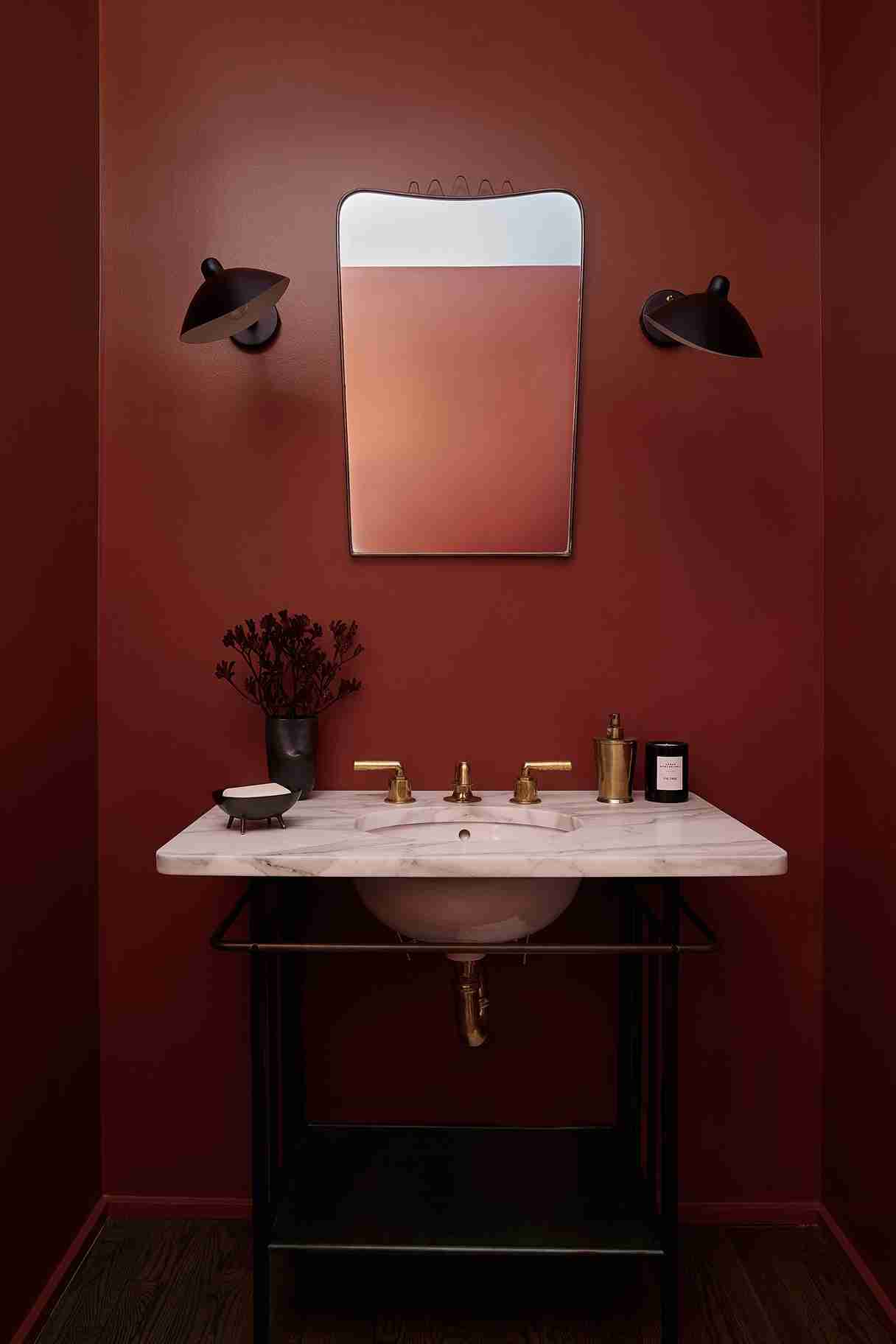 Small bathroom with slatted wood accent wall, white vanity, round backlit mirror, gray floor tiles, and pendant light creating a calm spa feel.